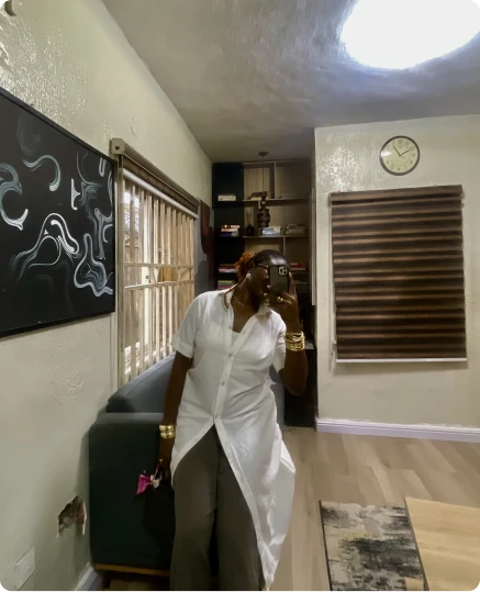 A woman in a white shirt taking a mirror selfie in a bright living room