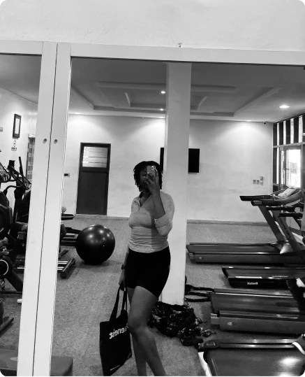 A woman in a gym with treadmills and an exercise ball, in black and white